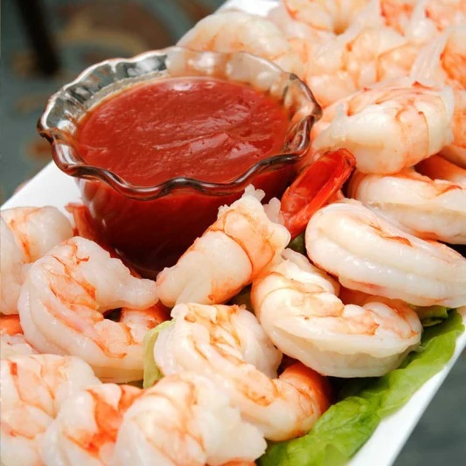 A close-up of a shrimp cocktail with a glass bowl of red sauce surrounded by cooked shrimp.