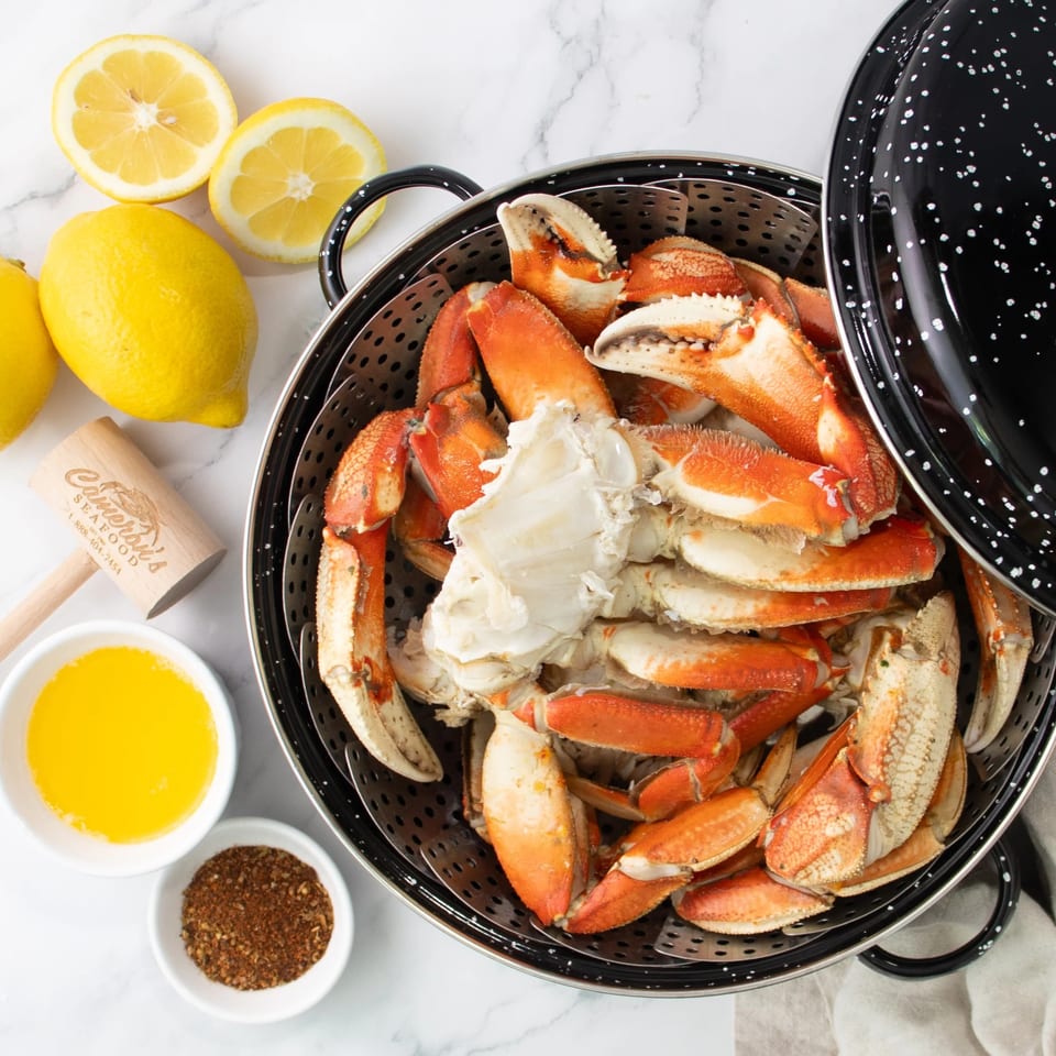 Steamed crab legs in a pot with lemons, melted butter, seasoning, and a crab mallet.